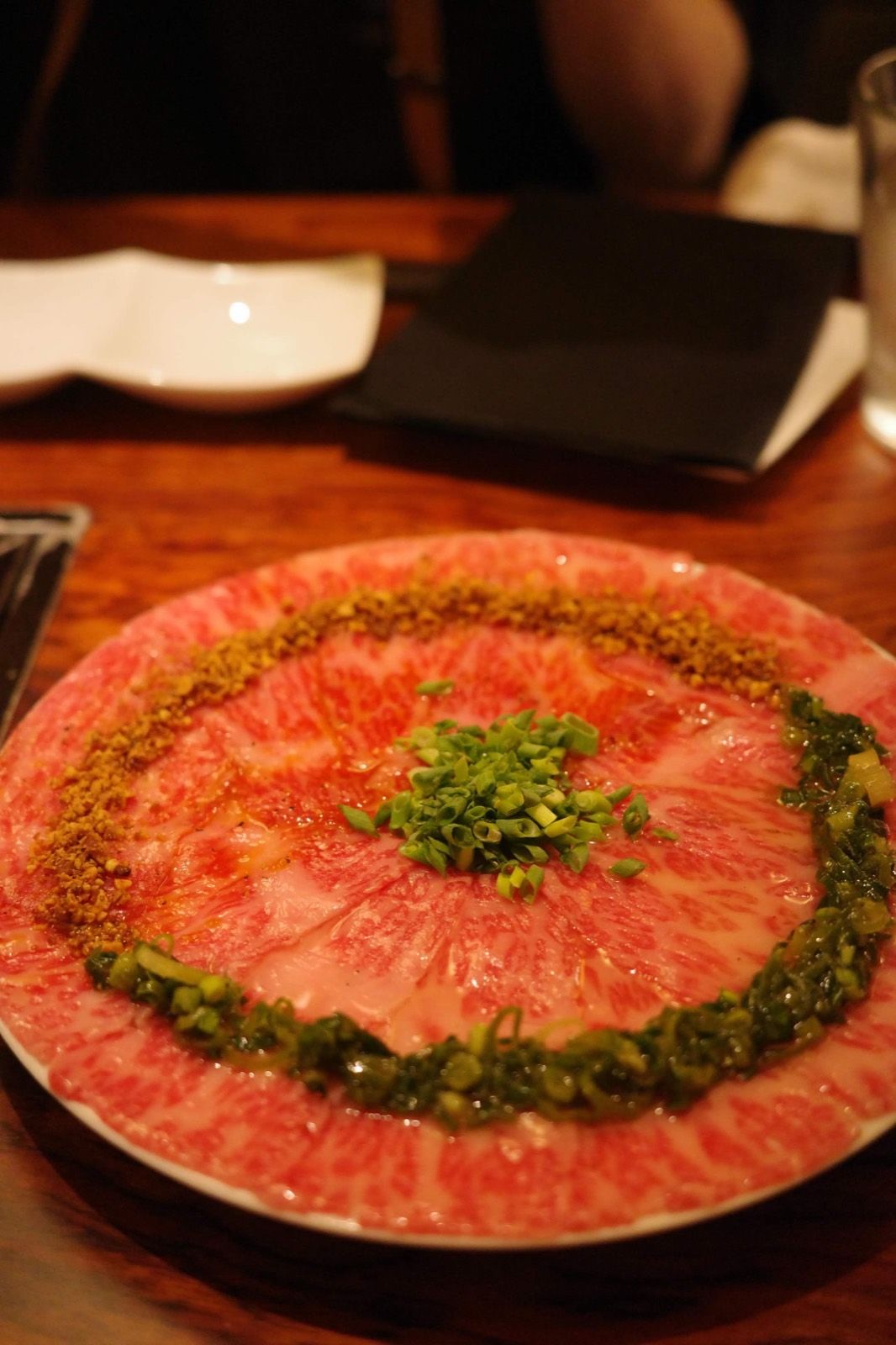Plate of thinly sliced marbled wagyu arranged in a circle, dressed with spring onion and crushed nuts.